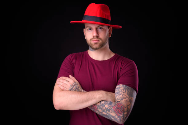 Young handsome bearded bald man with tattoos against black background