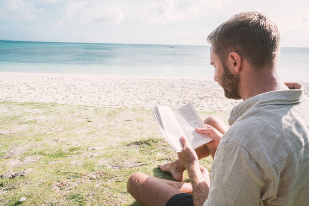 istock Young man reading book on tropical beach 925188628