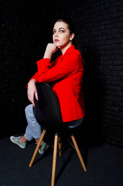 istock Stylish brunette girl on red jacket against studio black brick wall. 925190634