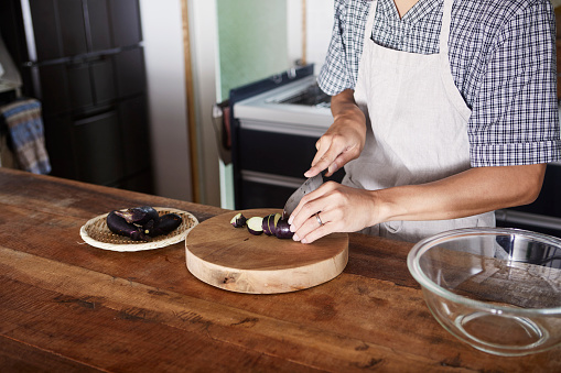 A man's hand cutting eggplants with a kitchen knife.