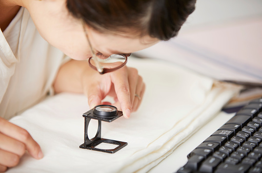 A woman looking at magnifying the fabric with a magnifying glass.