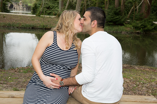 Happy young pregnant couple relaxing on beach river sitting together on bench