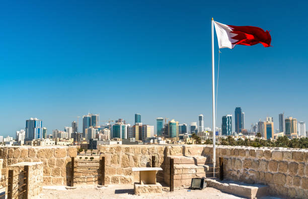 drapeau de bahreïn avec la ligne d’horizon de manama au bahreïn fort. patrimoine mondial de l’unesco - fort bay photos et images de collection
