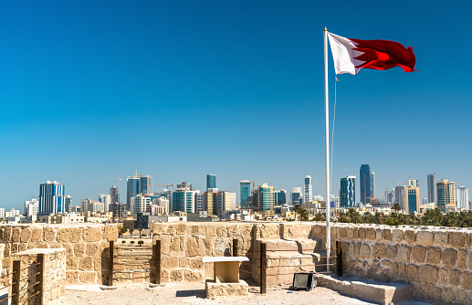 Bahrain Flag with skyline of Manama at Bahrain Fort. A UNESCO World Heritage Site in the Middle East