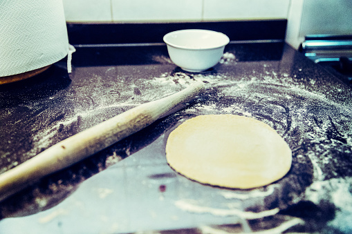 Close-up of rolling thin dough. The process of making dough for Ukrainian dumplings and other dough recipes. Beautiful view with a hand of raw homemade rolled dough on a light background