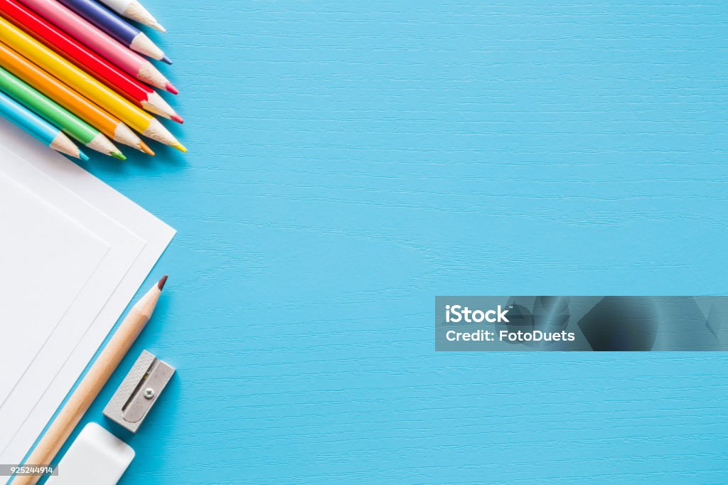 Colorful pencils, white papers and metal pencil sharpener. Empty place for text or drawing on the blue background. Childhood creative art concept. Flat lay. Education Stock Photo