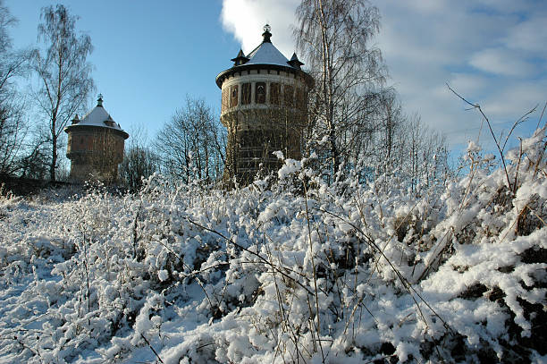 Frozen canal with snow, bare trees, and a water tower reflecting in the ice on a sunny winter day