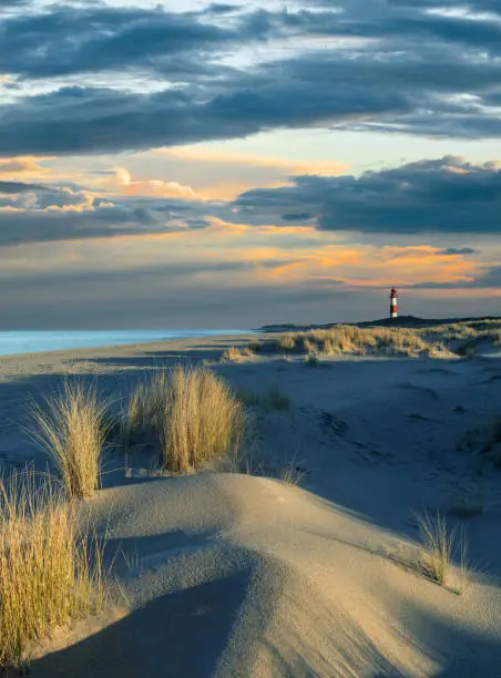 Sand dune and lighthouse in the north of island Sylt, Germany, at sunset with majestic cloudscape.