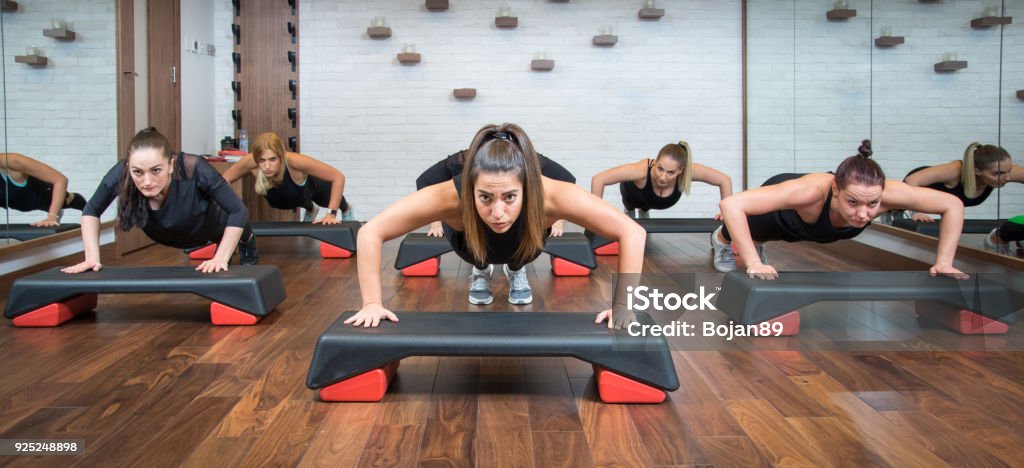 Group of fitness women doing push ups on aerobic stepper in gym. Exercise Class Stock Photo