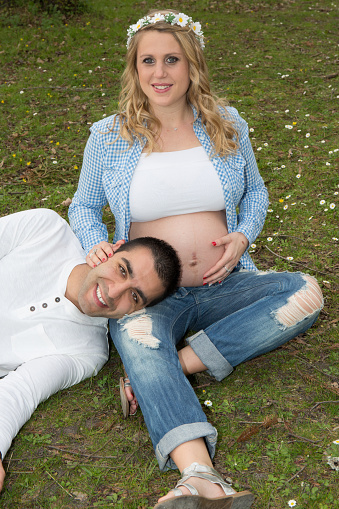 Happy beautiful pregnant woman with his husband sitting on the lawn outside