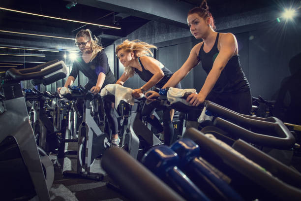 três meninas desportivos montando exercem motos juntos no ciclismo treino no ginásio. - pedal bicycle sports training cycling - fotografias e filmes do acervo