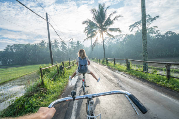Personal perspective- couple cycling near rice fields at sunrise, Indonesia Personal perspective of cheerful young couple cycling in the country side of Indonesia, Borobudur, Central Java, Indonesia. People travel recreational activities concept angle photos stock pictures, royalty-free photos & images