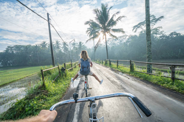 Personal perspective- couple cycling near rice fields at sunrise, Indonesia Personal perspective of cheerful young couple cycling in the country side of Indonesia, Borobudur, Central Java, Indonesia. People travel recreational activities concept central java province photos stock pictures, royalty-free photos & images