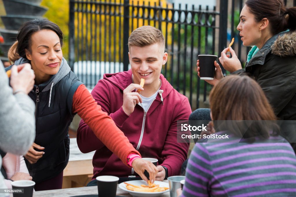 A Group Of Friend Eating Chips A group of friends sitting around a picnic table eating chips and drinking coffee Adult Stock Photo