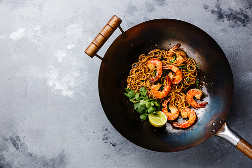 Ramen stir-fry noodles with shrimp in wok pan on gray concrete background copy space