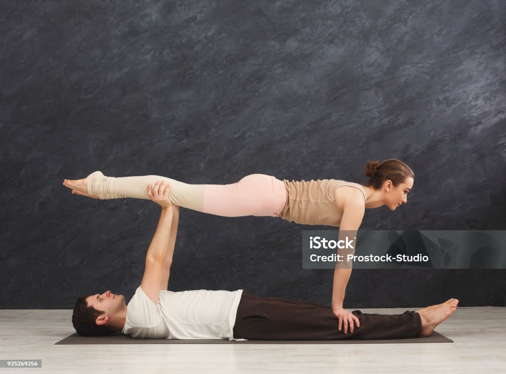 Young couple practicing acroyoga on mat together Young couple practicing acroyoga on mat in gym together. Woman doing plank pose, copy space, side view. Partner yoga, flexibility, trust concept Acroyoga Stock Photo