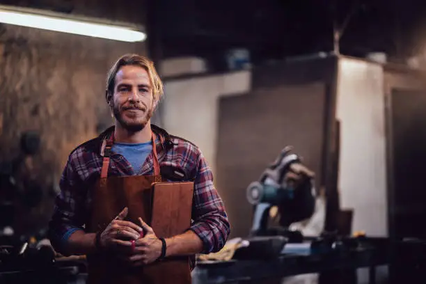 Young entrepreneur professional craftsman standing in workshop with laptop and coffee