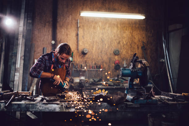 Craftsman cutting metal and using angle grinder in workshop Blacksmith working with power tools and cutting metal with angle ginder in workshop sharpening photos stock pictures, royalty-free photos & images