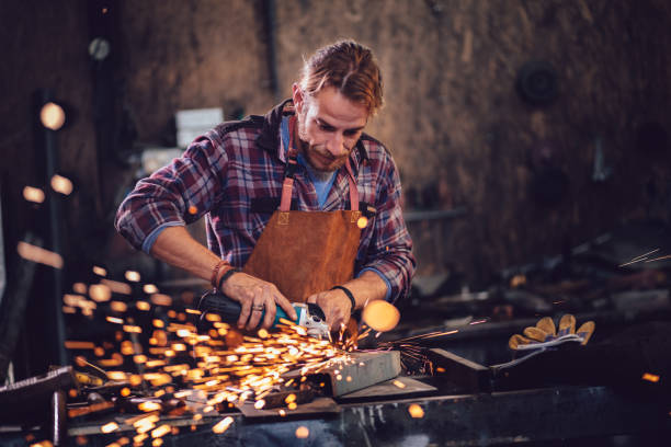 Blacksmith cutting metal with angle grinder in workshop Mechanic using angle grinder and cutting metal with sparks flying off in workshop garage blacksmith shop photos stock pictures, royalty-free photos & images