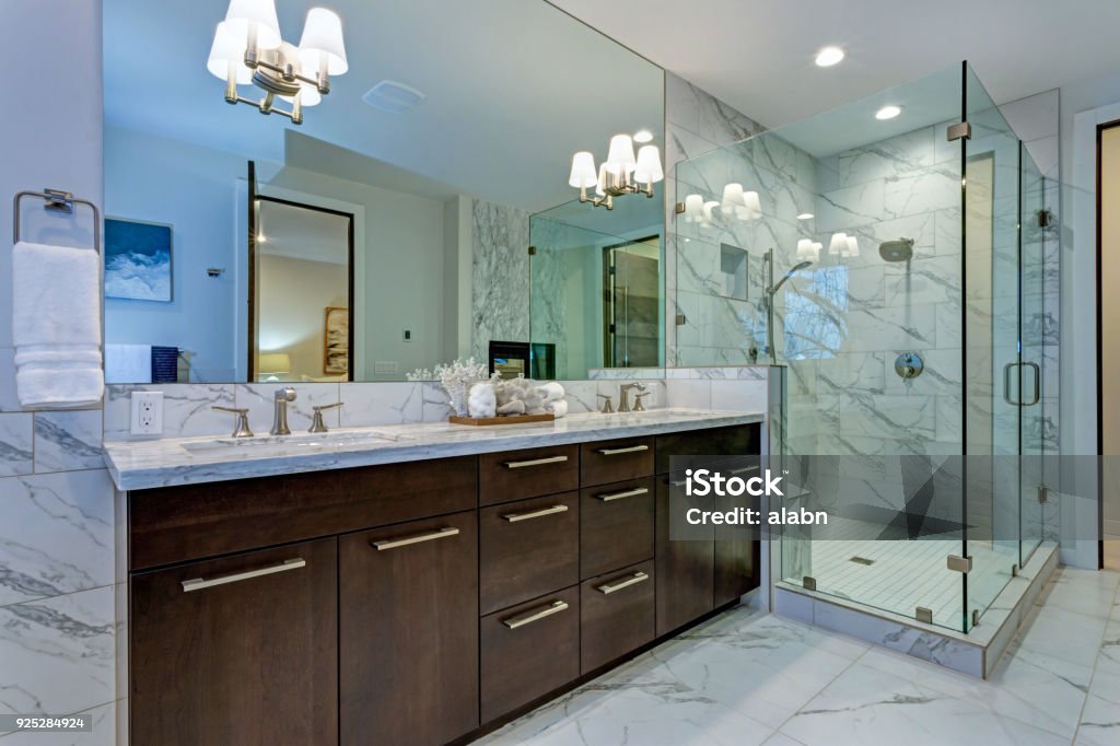Incredible master bathroom with Carrara marble tile surround. Incredible master bathroom with Carrara marble tile surround, modern glass walk in shower, espresso dual vanity cabinet and a freestanding bathtub. Shower Stock Photo