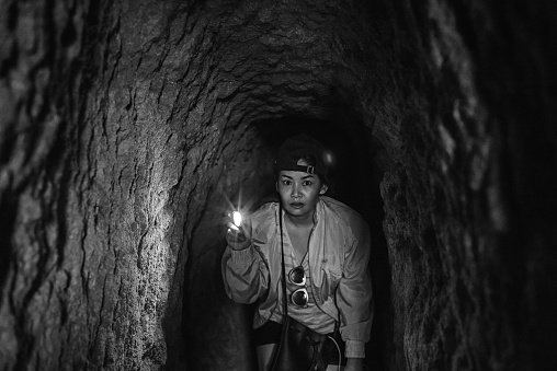 Asian woman holding small torch in dark old mine tunnel in black and white
