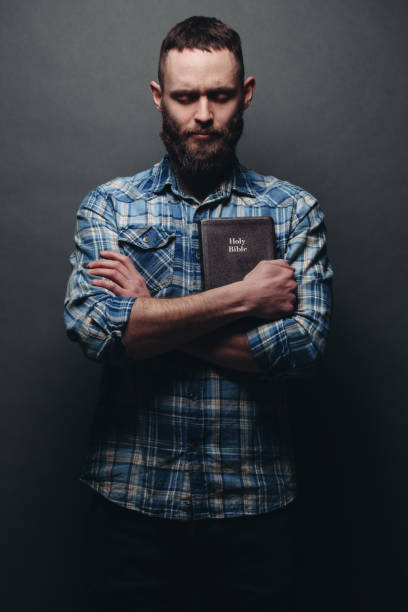 istock Handsome man reading and praying over Bible in a dark room over gray texture 925290654
