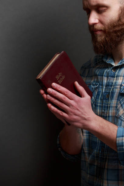 istock Handsome man reading and praying over Bible in a dark room over gray texture 925294464