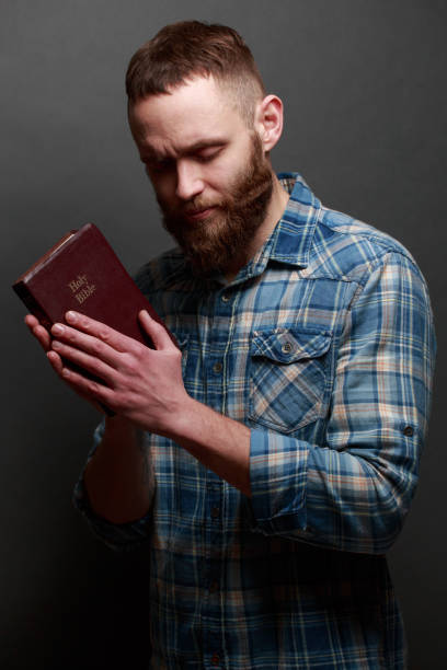 istock Handsome man reading and praying over Bible in a dark room over gray texture 925294814
