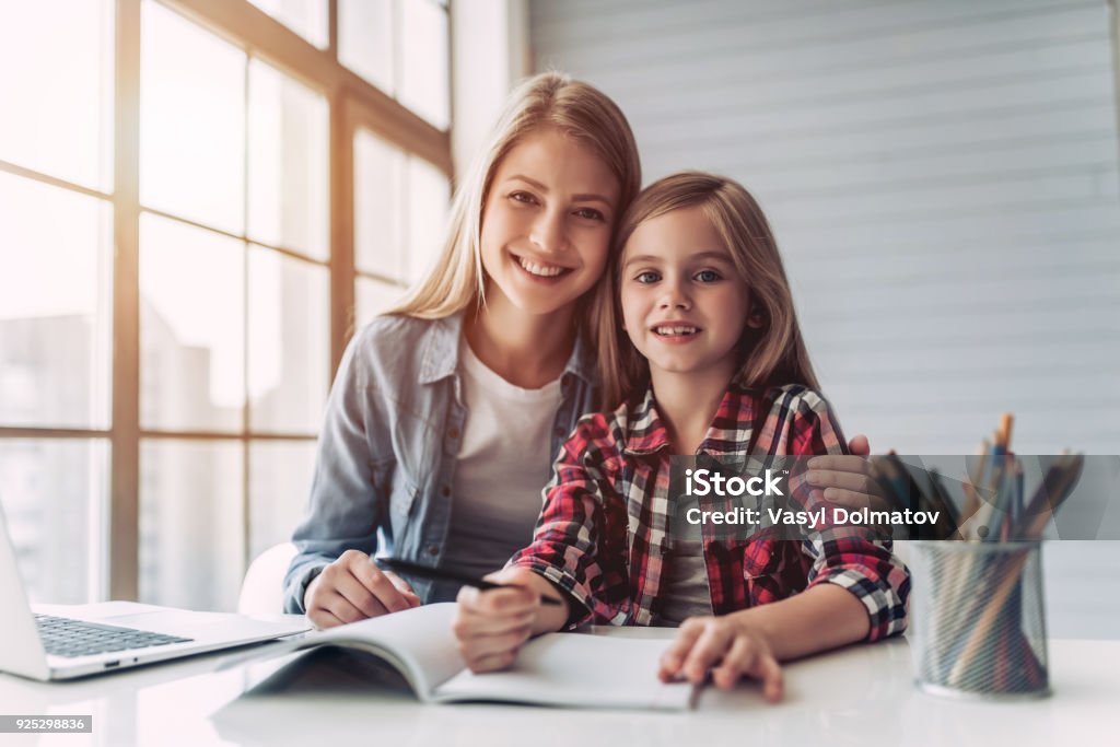 Mother with daughter Attractive young woman and her little cute daughter are sitting at the table and doing homework together. Mother helps daughter with her school classes. Homework Stock Photo