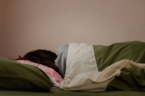 young woman is sleeping from the back in bed - women illness young women one person imagens e fotografias de stock