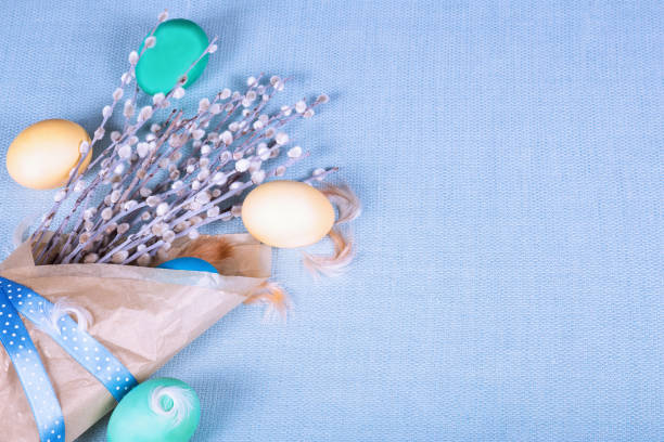 istock Paper package with pussy willow, painted eggs and feather on blue fabric tablecloth. Bright easter background. Top view. 925307964