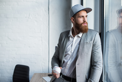 bearded businessman in baseball cap looking at window and holding baseball ball