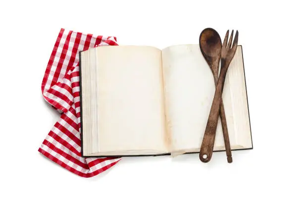 Open old cookbook with blank pages isolated on white background. A wooden spoon and a fork are on the open book at the right. The pages are weathered and shows stains and scratches. Copy space available for text and/or logo. High key DSRL studio photo taken with Canon EOS 5D Mk II and Canon EF 70-200mm f/2.8L IS II USM Telephoto Zoom Lens
