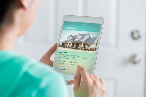 Woman uses digital table to search for new home Unrecognizable woman uses a digital tablet to shop for a new home. She is reading information about a two story home in the suburbs. real estate agent photos stock pictures, royalty-free photos & images