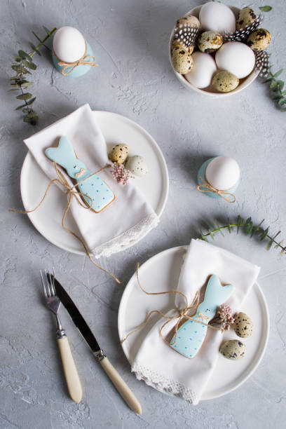 istock Easter  festive table setting with Easter bunny cookies, quail eggs  and chicken egg, green  leaf sprigs of eucalyptus. On a gray concrete background. Holiday celebration decorations. 925323482
