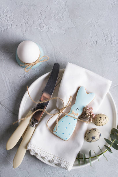 istock Easter  festive table setting with Easter bunny cookies, quail eggs  and chicken egg, green  leaf sprigs of eucalyptus. On a gray concrete background. Holiday celebration decorations. 925323542