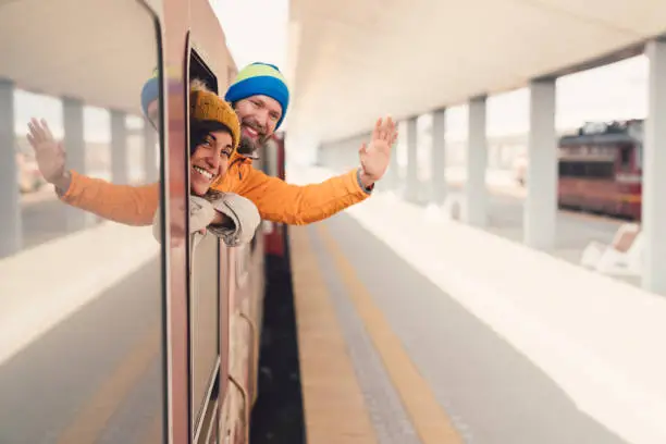 Young man with girlfriend waving with hand from the train