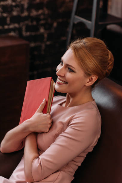 istock beautiful young woman embracing book while sitting on couch 925324430