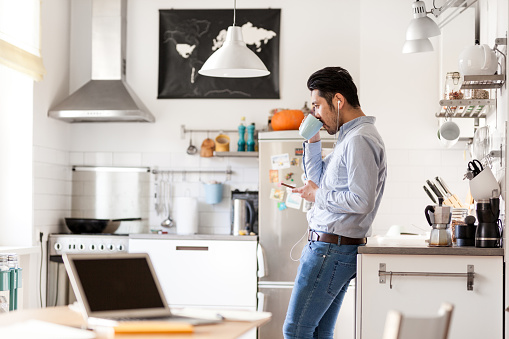 Japanese man in nordic style home is listening to podcast and making coffee.