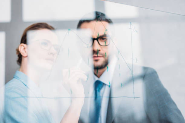 istock confident businesspeople drawing graphs on glass presentation board 925344014