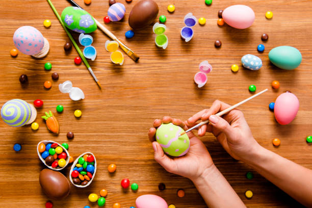 istock Top view portrait with copy space for text of easter elements, on wooden brown background laying small, little chocolate, carrot figure, paints, brush, woman's hands draw paint on egg 925349752
