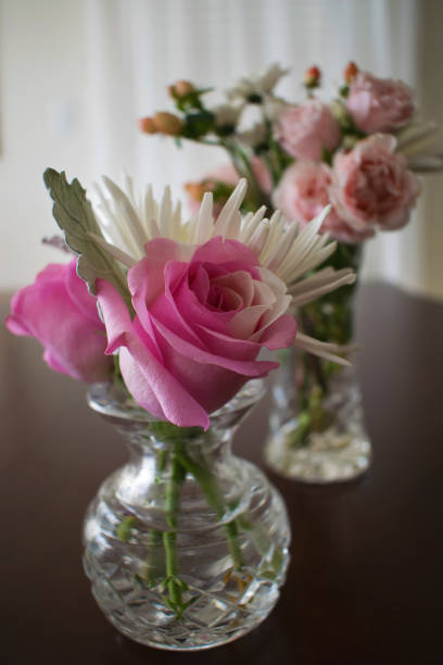 istock Two crystal vases with flowers on dark table window behind 925353124