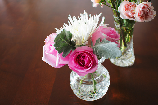 Two crystal vases with roses and other miniature flowers on dark wood dining room table.