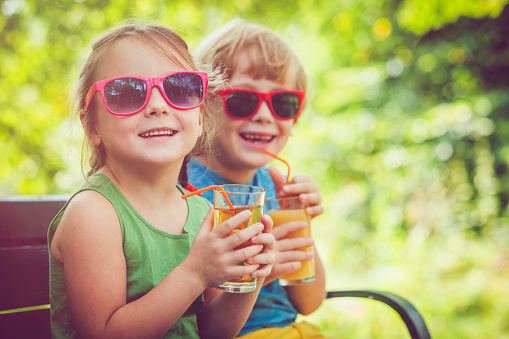 Happy boy and girl drinking juice outdoors in summer