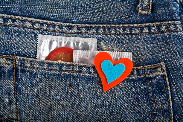 préservatifs colorés dans la poche de jeans bleu et coeur coloré - sex condom jeans horizontal photos et images de collection