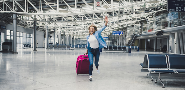 Attractive young woman is running in airport terminal with pink suitcase. Ready for traveling!