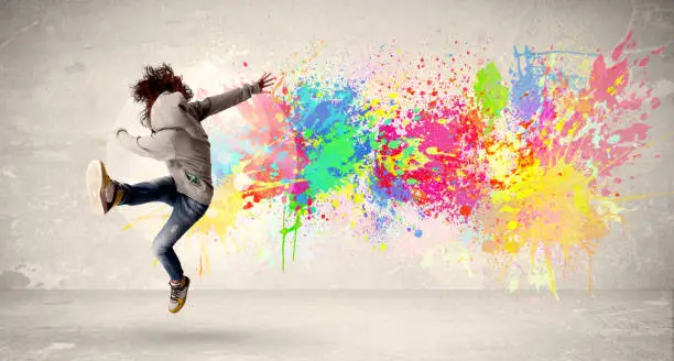 Photo of Happy teenager jumping with colorful ink splatter on urban background