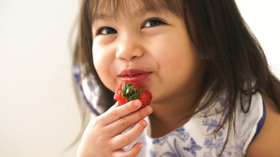 Niña bebé asiático es comer fresas en su habitación photo