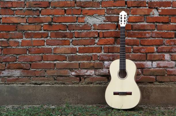 istock Acoustic guitar leaning on grunge red brick wall. Grass on pavement 925395830