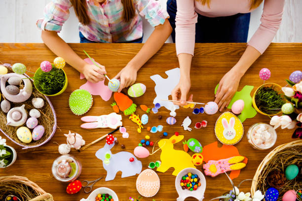 istock Top view of handmade easter objects, subjects, things, laying on wooden table, mother and daughter's hands painting, decorate eggs, holding brushed 925411068
